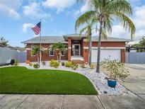 Charming single-story home with artificial grass, an American flag, and lush tropical landscaping at 1102 Goshen Rd, Tarpon Springs, FL 34689