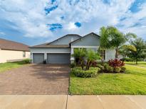 Charming single-Gathering home with a three-car garage, brick driveway, and tropical landscaping at 11714 Sunburst Marble Rd, Riverview, FL 33579