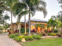 Charming single-story home featuring vibrant landscaping with palm trees, flowers, and a brick driveway at 6801 S Sparkman St, Tampa, FL 33616