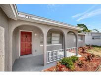 Home front entrance featuring a red door, gray stucco exterior and white accents at 7411 Seashore Dr, Port Richey, FL 34668