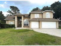 Two-story home featuring a three-car garage, tan paint, mature landscaping, and an arched entryway at 10402 Ashley Oaks Drive, Riverview, FL 33578