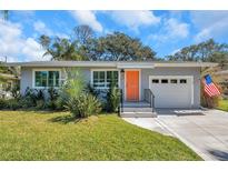 Charming single story home with a well-manicured lawn, bright orange door, and attached one car garage at 1841 Douglas Ave, Dunedin, FL 34698