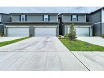 A row of gray two-story townhomes featuring individual garages and a concrete driveway at 32451 Limitless Pl, Wesley Chapel, FL 33545