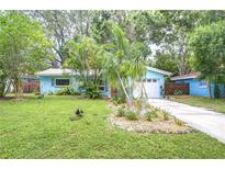 Charming blue home with lush landscaping and a well-manicured lawn, set among mature trees, creating a tranquil oasis at 2051 Indigo Dr, Clearwater, FL 33763