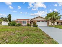 Charming brick home with a well-maintained lawn, arched entryway, and two-car garage, under a partly cloudy, blue sky at 326 Circle Dr, Palm Harbor, FL 34683