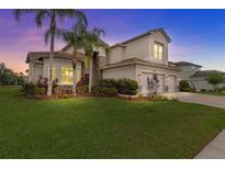 Stunning two-story home with a three-car garage, lush landscaping, and mature palm trees at sunset at 2724 Coco Palm Cir, Wesley Chapel, FL 33543