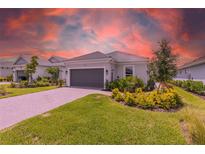 Charming single-story home featuring manicured landscaping, a gray two-car garage door, and a paver driveway at 16126 San Donato Pl, Bradenton, FL 34211