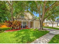 Charming two-story home featuring a manicured lawn, lush trees, and a welcoming front porch with decorative plants at 8514 Manassas Rd, Tampa, FL 33635