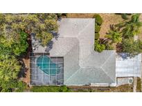 Aerial view of a home featuring a screened-in pool and a well-maintained gray shingle roof surrounded by lush landscaping at 7613 Bramblewood Dr, Port Richey, FL 34668