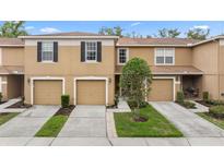 Tan townhome featuring attached garages, a manicured lawn, and welcoming curb appeal at 4149 Winding River Way, Land O Lakes, FL 34639