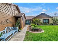 Charming home featuring a well-manicured lawn, lush landscaping, and inviting entryway with a comfortable, light blue bench at 2475 Bay Berry Dr, Clearwater, FL 33763