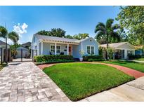 Charming blue home boasts lush landscaping, a brick walkway, and an inviting front porch with seating at 115 S Beverly Ave, Tampa, FL 33609
