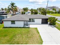 Inviting single-story home with a spacious front yard, a black garage door, and a concrete driveway at 13715 Maria Dr, Hudson, FL 34667