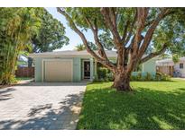 Charming single-story home featuring a well-manicured lawn, paver driveway, and a large shade tree at 1281 Robin Hood Ln, Dunedin, FL 34698