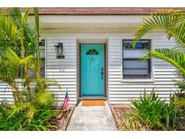 Charming white home exterior features a vibrant turquoise front door surrounded by lush, tropical landscaping at 9142 Oakwood Ln, Seminole, FL 33776