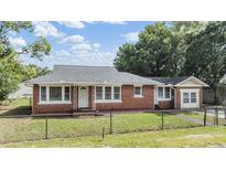 Charming brick home with a well-manicured lawn and black chain link fence under a blue sky at 1511 Emma E St, Tampa, FL 33610