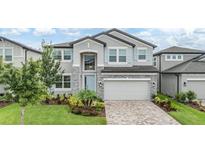Two-story home with stone accents, a manicured lawn, paver driveway, and light blue shutters at 7276 Notched Pine Bnd, Wesley Chapel, FL 33545