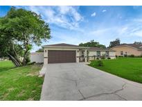 Charming single-story home features a two car garage, well-manicured lawn, and mature tree in the front yard at 5015 Summer Hill Dr, Zephyrhills, FL 33542
