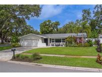 Charming single-story home featuring a lush green lawn and mature trees, with a brick-paved driveway at 1368 Whispering Pines Dr, Clearwater, FL 33764