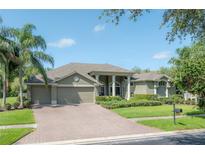 Well-maintained, tan-colored home with columns, a three-car garage, green grass, and a brick driveway at 27528 Water Ash Dr, Wesley Chapel, FL 33544