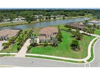 Stunning aerial view of a lakeside property with lush landscaping, a paver driveway, and a red tile roof at 4973 Antiquity Way, Sarasota, FL 34240