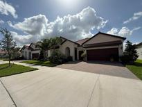 Beautiful single-story home featuring a tile roof, arched entry, brick driveway, and well-manicured landscaping at 17304 Scuba Crest St, Wimauma, FL 33598