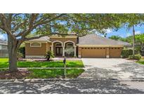 Charming single-story home with manicured lawn, mature trees, and a three-car garage on a sunny day at 5519 Reflections Blvd, Lutz, FL 33558
