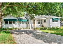 Charming white home with green awnings and a beautiful brick driveway framed by mature trees and lush landscaping at 4616 S Matanzas Ave, Tampa, FL 33611