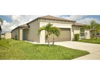Beige single-story home featuring a two-car garage, palm trees, and a well-manicured lawn at 16623 Carlton Pond St, Wimauma, FL 33598