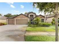 Charming single-Gathering home featuring a stone facade, three-car garage, and lush landscaping at 12729 Flatwood Creek Dr, Gibsonton, FL 33534