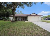 Charming single-story home with a well-maintained lawn, mature tree and an attached two-car garage at 13013 Sawmill Way, Hudson, FL 34667