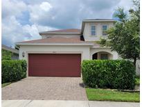 Two-story home featuring a brick driveway, well-maintained landscaping and a red two-car garage door at 7563 Ashcroft Dr, Wesley Chapel, FL 33545