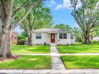 Charming single story home featuring a red front door, well-manicured lawn, and mature shade trees at 1243 55Th N Ave, St Petersburg, FL 33703