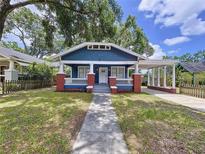Charming blue home featuring a cozy front porch with classic brick accents and a convenient covered parking area at 1019 E Mohawk Ave, Tampa, FL 33604