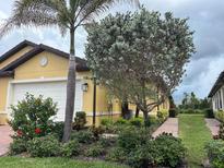 Charming yellow home featuring lush landscaping, brick walkway, and mature palm trees for a tropical feel at 21008 Fetterbush Pl, Venice, FL 34293