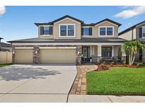 Charming two-story home featuring a three-car garage, stone accents, and manicured lawn at 7570 Sweeter Tide Trl, Wesley Chapel, FL 33545