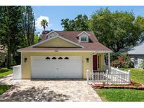 Charming, light yellow home featuring a brick paved driveway, a manicured lawn, and a white picket fence at 346 Gray Oak Dr, Tarpon Springs, FL 34689