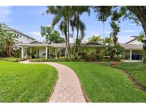 Charming single-story home with lush landscaping, brick walkway, and tropical palm trees in the front yard at 648 Geneva Pl, Tampa, FL 33606