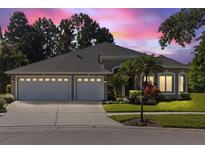 Charming home featuring a well-manicured lawn, mature trees, and a three-car garage at twilight at 10751 Tavistock Dr, Tampa, FL 33626