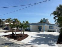 Charming single-story home featuring blue accents, a spacious driveway, and lush landscaping with mature palm trees at 11110 1St E St, Treasure Island, FL 33706
