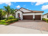 Charming home boasts a three-car garage, terracotta roof, lush landscaping, and a brick paved driveway at 16938 Scuba Crest St, Wimauma, FL 33598