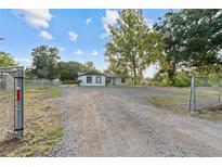 Wide shot of a white, one-story home with a gravel driveway and fenced yard at 221 S Kingsway Rd, Seffner, FL 33584