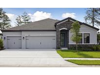 Charming home featuring a three-car garage, stone accents, and a well-manicured lawn at 3448 Yellow Leaf Cir, Spring Hill, FL 34609