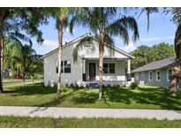 Charming white home with a manicured green lawn, palm trees and inviting front porch with black trim at 5709 N 20Th St, Tampa, FL 33610