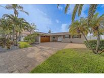 Charming single-story home featuring a spacious brick driveway, lush lawn, and mature tropical landscaping at 735 123Rd Ave, Treasure Island, FL 33706