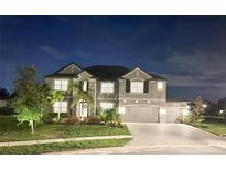 Night view of a two-story home featuring stone accents, a three-car garage, and manicured landscaping at 9508 Pyrenees Pl, Seffner, FL 33584