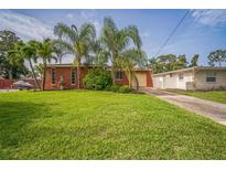 Charming home with a large grassy front yard, palm trees, and a driveway leading to a garage at 51 Cypress Dr, Palm Harbor, FL 34684