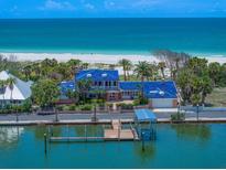 Stunning beachfront home with a blue tile roof, private dock, and lush landscaping, offering direct access to the ocean at 1114 Mandalay Pt, Clearwater Beach, FL 33767