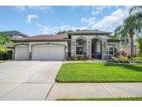 Charming home with a three-car garage, stone accents, lush landscaping, and well-manicured lawn at 12918 Tar Flower Dr., Tampa, FL 33626