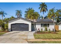 Charming single-story home showcasing a brick facade, dark garage door, and lush landscaping with mature palm trees at 6000 Denver Ne St, St Petersburg, FL 33703